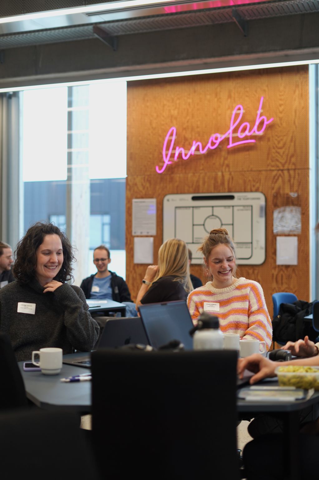 Pitch Bootcamp participants listening around a table with laptops.